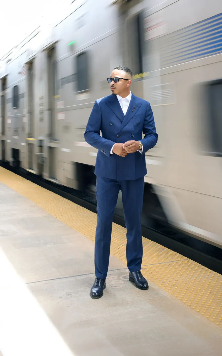 Navy double-breasted suit on a station platform, train passing