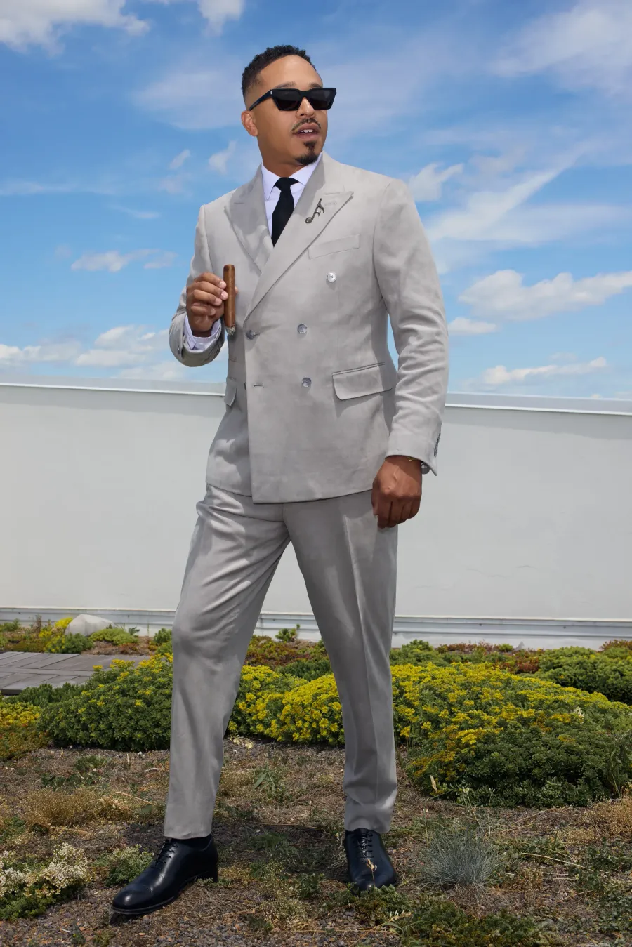 Stone grey double-breasted suit on a rooftop, cigar in hand