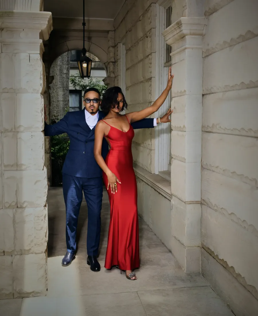 Couple under a stone colonnade — navy suit and red satin gown