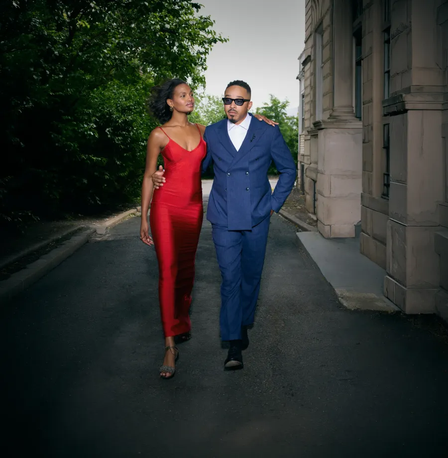 Couple walking a sunlit street — red gown and navy suit